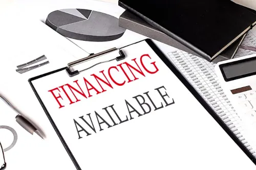 A desk filled with various items including a pen, graph, calculator, and a clipboard displaying "financing available."