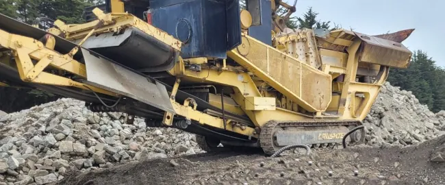 A big yellow 2017 Hartl 1470I crusher positioned on a dirt field, surrounded by large piles of rocks.