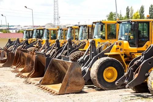 A lineup of nine yellow bulldozers parked on a large open lot.