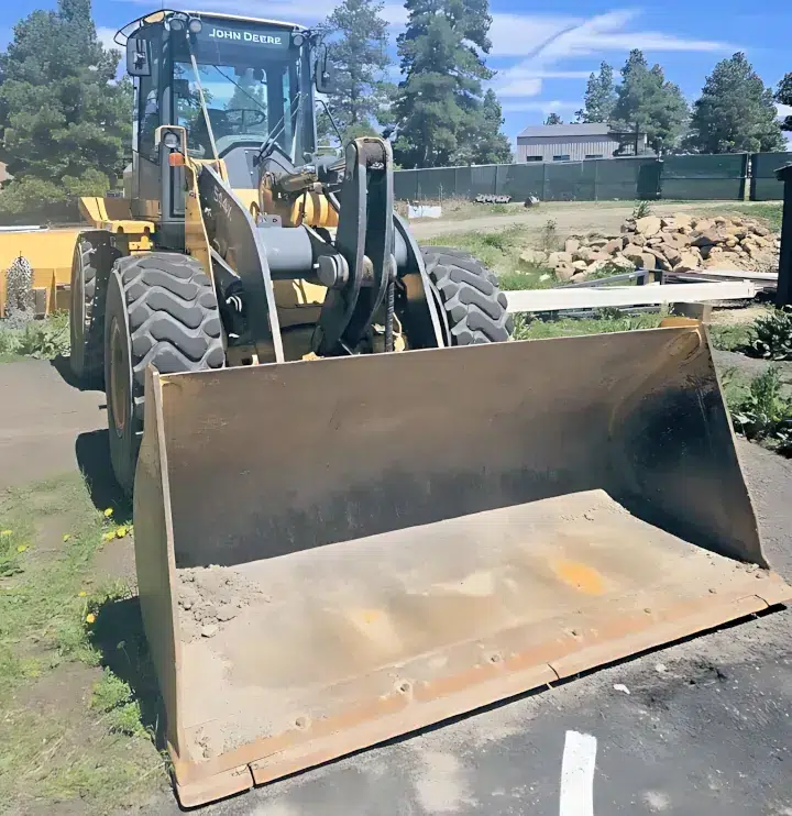 Yellow John Deere 544K compact wheel loader featuring a heavy-duty front bucket, stationed in an empty lot.