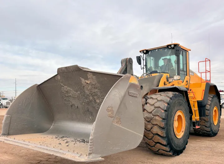 A robust yellow 2016 Volvo L220H wheel loader, built for mining and construction, being operated in a parking lot.
