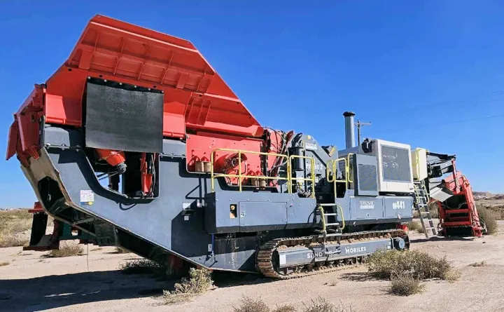 A 2019 Sandvik QI441 impact crusher featuring a red upper section, positioned alone on an empty lot.