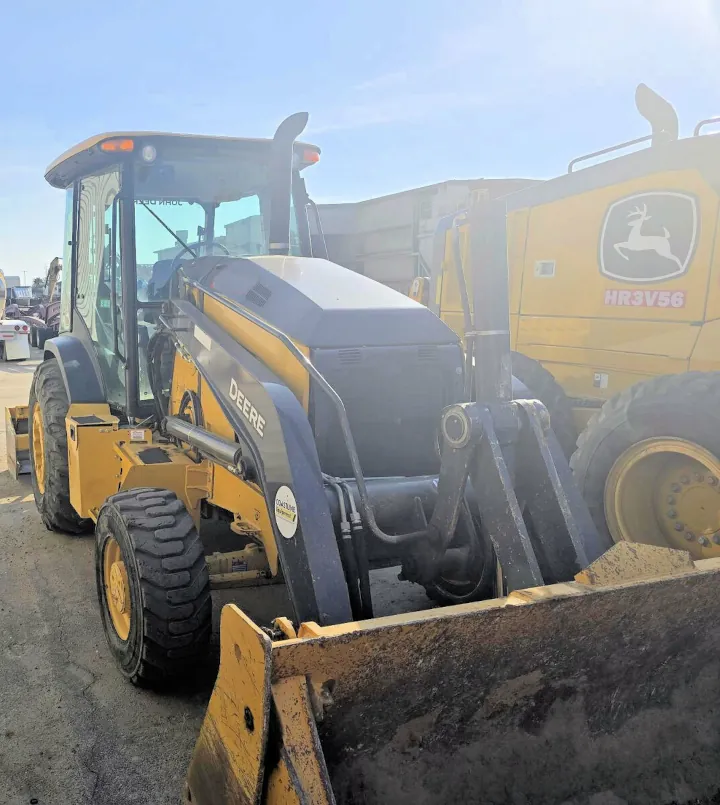 A compact yellow 2020 John Deere 210L skip loader, built for landscaping and material handling, is parked among numerous machines in a lot.