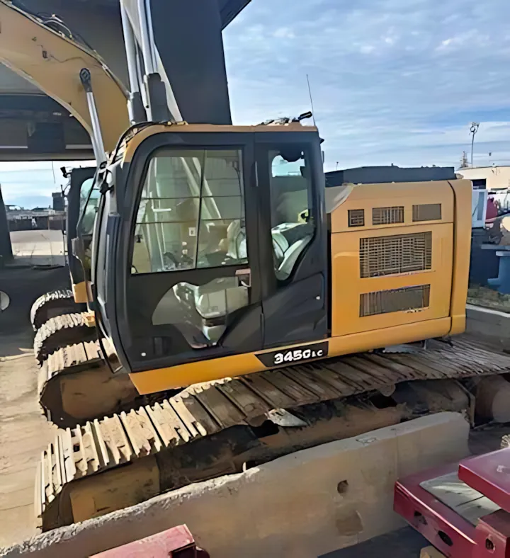 A medium-sized yellow 2022 John Deere 345G LC excavator, designed for urban job sites, is parked on a concrete lot.